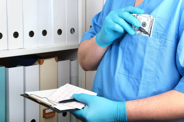 Arzt in blauer Uniform schreibt auf den Rohling auf dem Hintergrund eines Regals mit Ordnern. Bestechung und Korruption Konzept, Bestechung in Form von Dollarscheinen, — Stockfoto