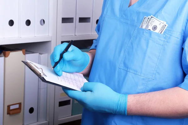 O doutor em um uniforme azul escreve ao branco em um contexto de uma prateleira com pastas. Concepção de suborno e corrupção, suborno na forma de notas de dólar , — Fotografia de Stock