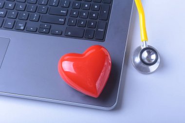 İşyeri dizüstü bilgisayar, stetoskop, kırmızı kalp ve beyaz masa üstünde defter doktor. Üstten Görünüm.