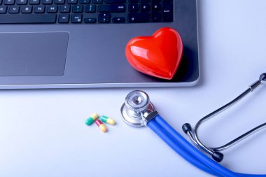 İşyeri dizüstü bilgisayar, stetoskop, kırmızı kalp ve beyaz masa üzerinde çeşitli pils doktor. Üstten Görünüm.
