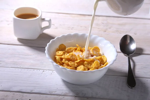 Milk pouring into a bowl of delicious corn flake cereals and cap with espresso coffee. Morning breakfast. — Stock Photo, Image