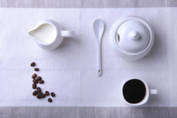 Cup of hot coffee espresso, coffee beans, jug of milk, and bowl with sugar on white background for copy space. Coffee concept.