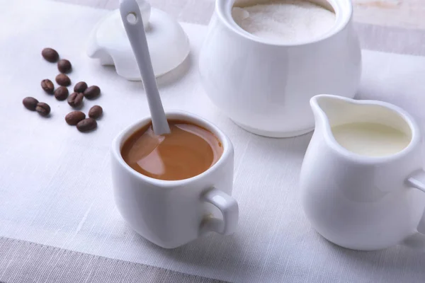 Cup of hot coffee espresso, coffee beans, jug of milk, and bowl with sugar on white background for copy space. Coffee concept.