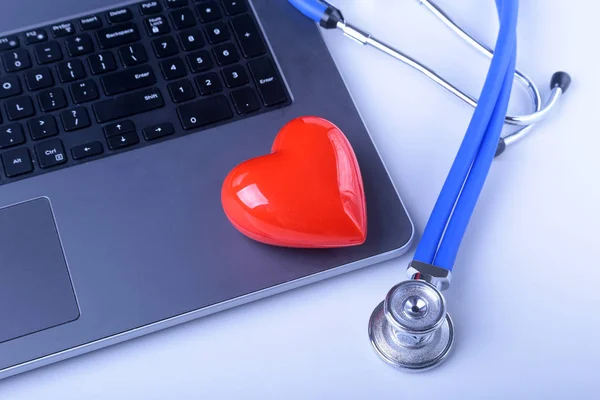 Lugar de trabajo del médico con portátil, estetoscopio, corazón rojo y portátil en la mesa blanca. vista superior . — Foto de Stock