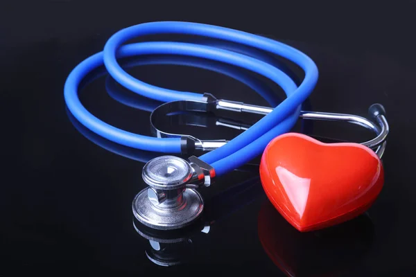 Stethoscope, Red heart and blood pressure meter on black mirror background. Selective focus. — Stock Photo, Image