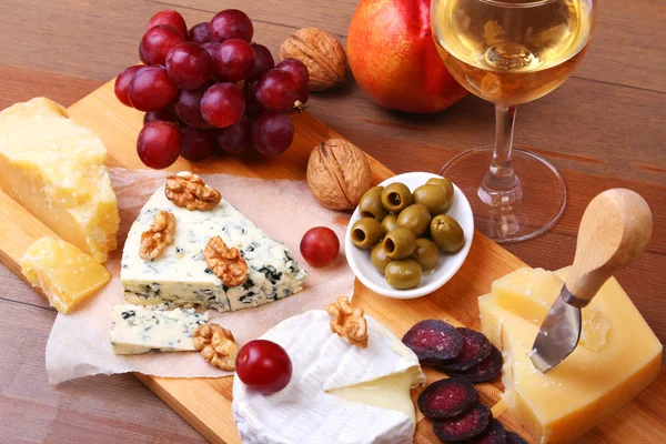 Surtido de queso con frutas, uvas, frutos secos y cuchillo de queso en una bandeja de servir de madera . — Foto de Stock