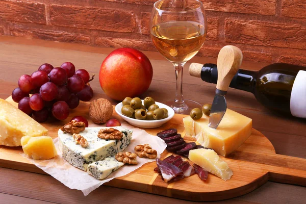 Sortimento de queijo com frutas, uvas, nozes e faca de queijo em uma bandeja de serviço de madeira . — Fotografia de Stock