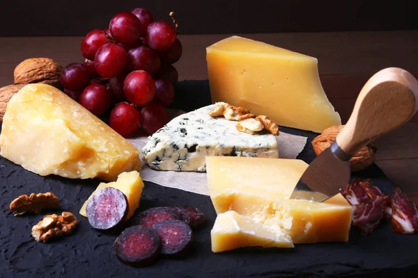 Çeşitli peynirler, fındık, üzüm, meyve, füme et ve servis masasında bir bardak şarap. Karanlık ve Moody tarzı. Metin için boş alan. — Stok fotoğraf
