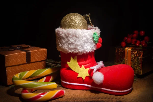 Rote Weihnachtsstiefel mit Weihnachtsgeschenken, Lollypop und Dekorationskugeln auf dunklem Hintergrund. frohe Feiertage. Stockbild