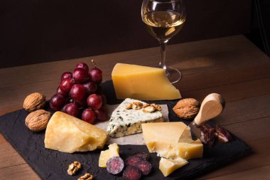 Çeşitli peynirler, fındık, üzüm, meyve, füme et ve servis masasında bir bardak şarap. Karanlık ve Moody tarzı. Metin için boş alan.