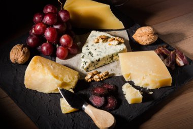 Çeşitli peynirler, fındık, üzüm, meyve, füme et ve servis masasında bir bardak şarap. Karanlık ve Moody tarzı. Metin için boş alan.