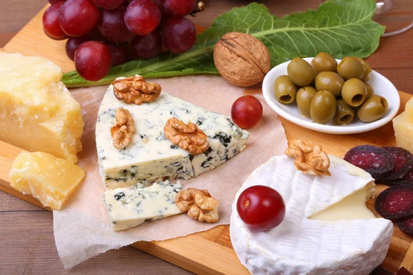 Ассортимент сыра с фруктами, виноградом, орехами, бокалом с вином и сырным ножом на деревянной подаче. — стоковое фото