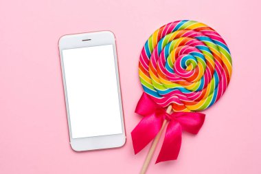 Pembe arka planda renkli lolipop ve cep telefonu, tekoloji ve çocuk tatlıları