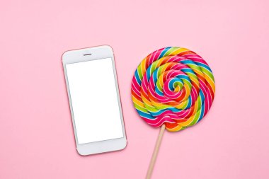 Pembe arka planda renkli lolipop ve cep telefonu, tekoloji ve çocuk tatlıları