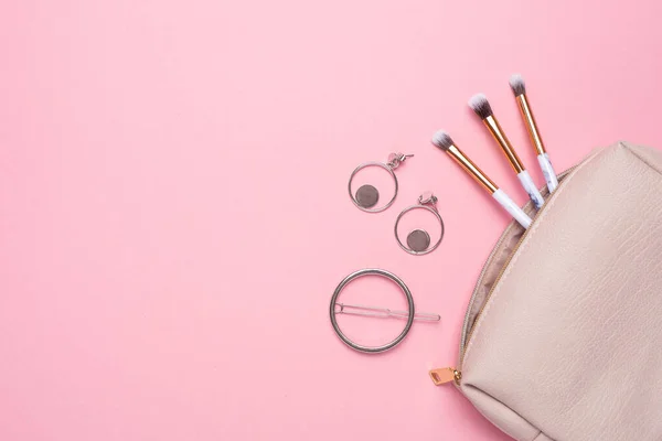 Makyaj fırçası ve küpeli kadın kozmetik çantası. Mesajınız için pembe bir arka plan.