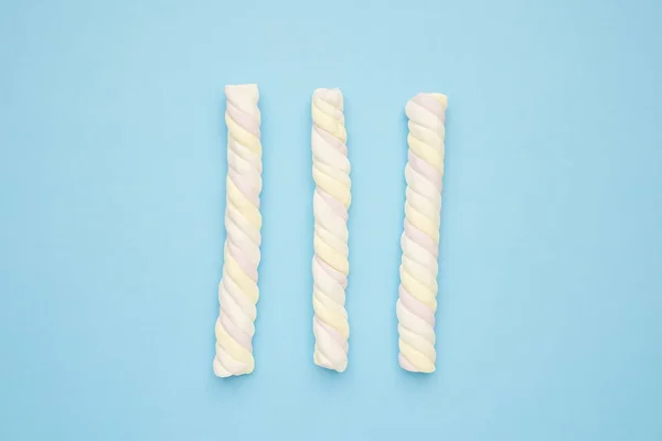Farbige lange Marshmallows auf blauem Hintergrund, köstliche Süßigkeiten flach liegend — Stockfoto