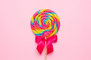 Pembe arka planda ahşap çubuklu renkli lolipop spirali, çocukluk tatlısı