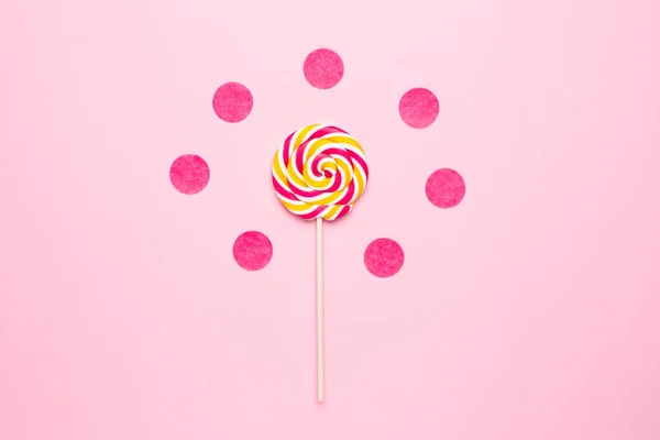 Colorful lolipop with wooden stick, pink, yellow and white spiral on pink background , childhood sweets — Stock Photo, Image