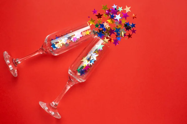Ποτήρια σαμπάνιας με χρωματιστά αστέρια κομφετί σε κόκκινο χρώμα φόντο χαρτί minimal στυλ — Φωτογραφία Αρχείου