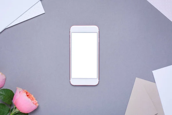 Gri arka planda pembe gül olan cep telefonu ve zarf