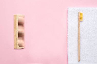 Eko ahşap diş fırçası, tarak ve beyaz banyo havlusu. Pembe arka planda, telif alanı, banyo ve spa aksesuarlı.