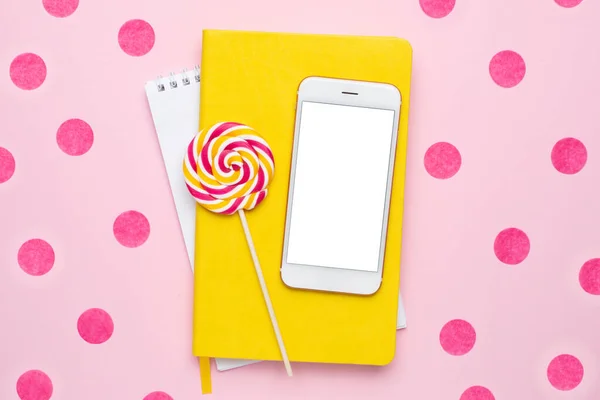 Handy mit gelbem Notizbuch und buntem Lolipop auf rosa Hintergrund mit Konfetti — Stockfoto