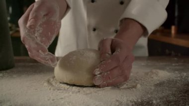 Erkek aşçı mutfakta un ile hamur hazırlıyor. Un serpiştirilmiş ekmek hamuru, yavaş çekimde yan görüşte pişiyor.