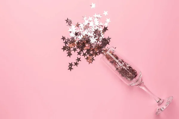 Champagne glass with silver pink stars confetti on pink color paper background minimal style