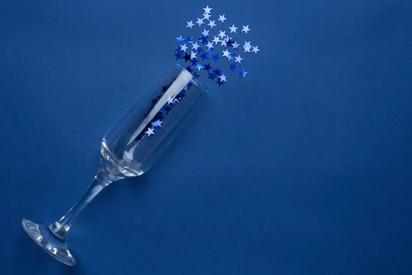 Ποτήρι σαμπάνιας με ασημένια μπλε αστέρια κομφετί σε κλασικό μπλε χρώμα φόντο minimal style — Φωτογραφία Αρχείου