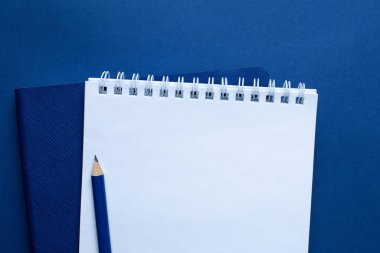 Klasik mavi arka planda beyaz, mavi ofis defteri ve kalem. Moda rengi 2020