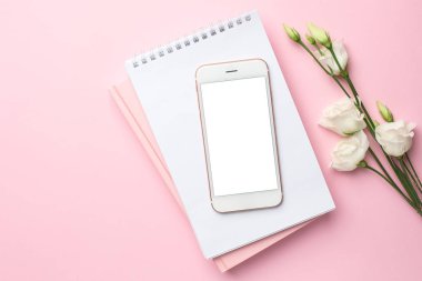 Cep telefonu, beyaz Eustoma çiçeği ve pembe arka planda bir defter. Kadın iş teknolojisi kompozisyonu