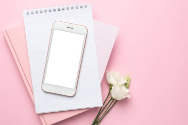 Cep telefonu, beyaz Eustoma çiçeği ve pembe arka planda bir defter. Kadın iş teknolojisi kompozisyonu