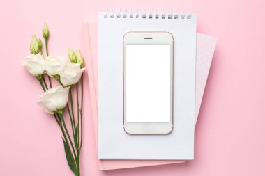 Cep telefonu, beyaz çiçek ve pembe arka planda bir defter. Kadın iş teknolojisi kompozisyonu