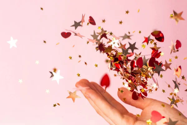 Confiti estrella de oro en la mano de las mujeres en el fondo de color rosa pastel. Fondo de vacaciones brillante y festivo . — Foto de Stock