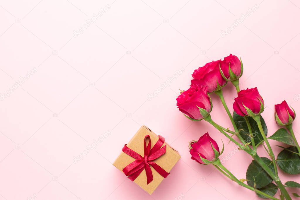 Pink roses flowers and present gift on pink background with copyspace. Minimalistic composition for Valentine's day day and holidays.