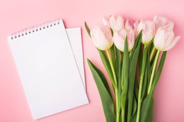 Not defteri ve bahar çiçeği pembe laleler pembe arka planda kopyalanmış. Aşk teması, Anneler Günü, Kadınlar Günü düzlük