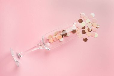 Pembe ve altın konfetili şampanya bardağı. Pembe renkli kâğıt arka planda. Üstten görünüm çok az.
