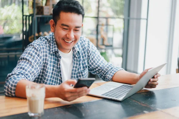 Asian young man in blue shirt working with laptop computer and m — Stock Photo, Image