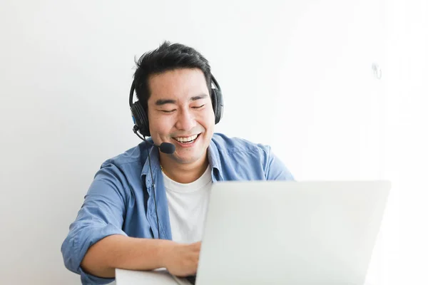 Asian handsome man in blue shirt using laptop with headphone tal — Stock Photo, Image