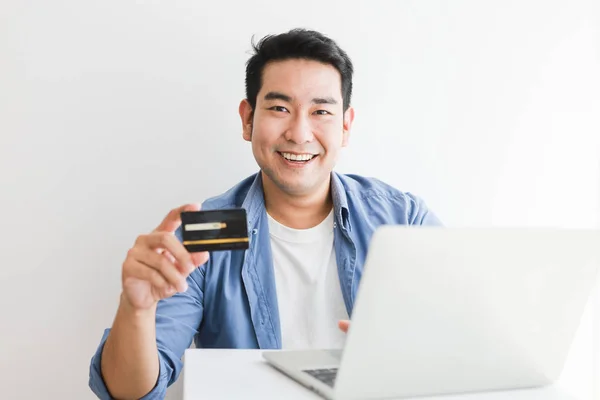 Asiático guapo hombre en azul camisa usando tarjeta de crédito con portátil c —  Fotos de Stock