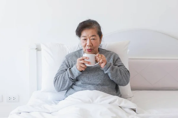 Asiatische senior alte Frau trinken Kaffee oder Tee auf die Bett — Stockfoto
