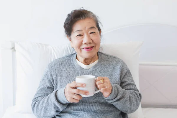 Asiatische senior alte Frau trinken Kaffee oder Tee auf die Bett — Stockfoto