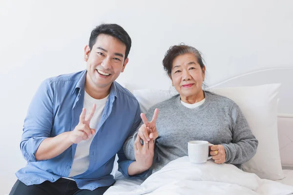 Asian senior old woman drinking coffee or tea on the bed