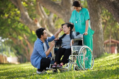 Asyalı son sınıf öğrencisi oğlu mutlu bir şekilde tekerlekli sandalyede oturuyor.