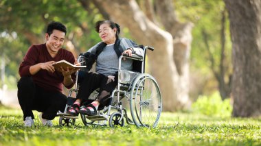 Asyalı son sınıf öğrencisi oğlu mutlu bir şekilde tekerlekli sandalyede oturuyor.
