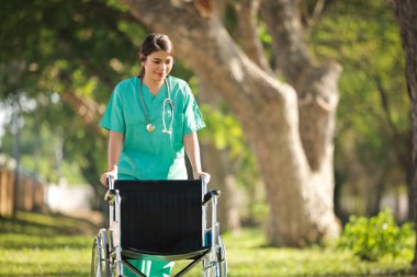 Hastane parkında tekerlekli sandalyeli, doktor üniformalı bir Asyalı kadın.
