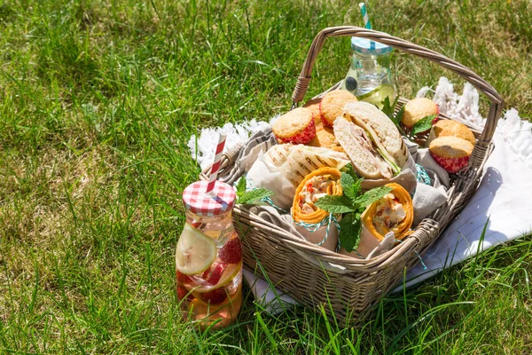 Cesta de piquenique com comida no gramado ensolarado verde — Fotografia de Stock