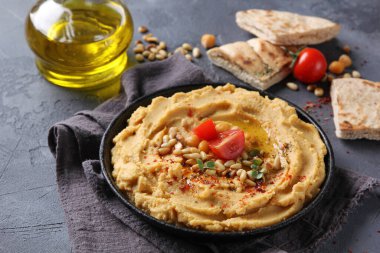 Doğu mutfağı kavramı. Zeytinyağı, baharat, çam fıstığı ve tortilla ile humus. Gri arka planda siyah bir tabakta nohut aperatifi. Türk bezelyesi. Arkaplan resmi, alanı kopyala