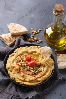 Doğu mutfağı kavramı. Zeytinyağı, baharat, çam fıstığı ve tortilla ile humus. Gri arka planda siyah bir tabakta nohut aperatifi. Türk bezelyesi. Arkaplan resmi, alanı kopyala