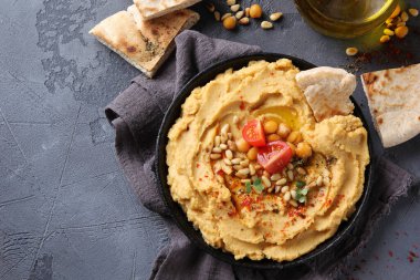 Doğu mutfağı kavramı. Zeytinyağı, baharat, çam fıstığı ve tortilla ile humus. Gri arka planda siyah bir tabakta nohut aperatifi. Türk bezelyesi. Arkaplan resmi, alanı kopyala